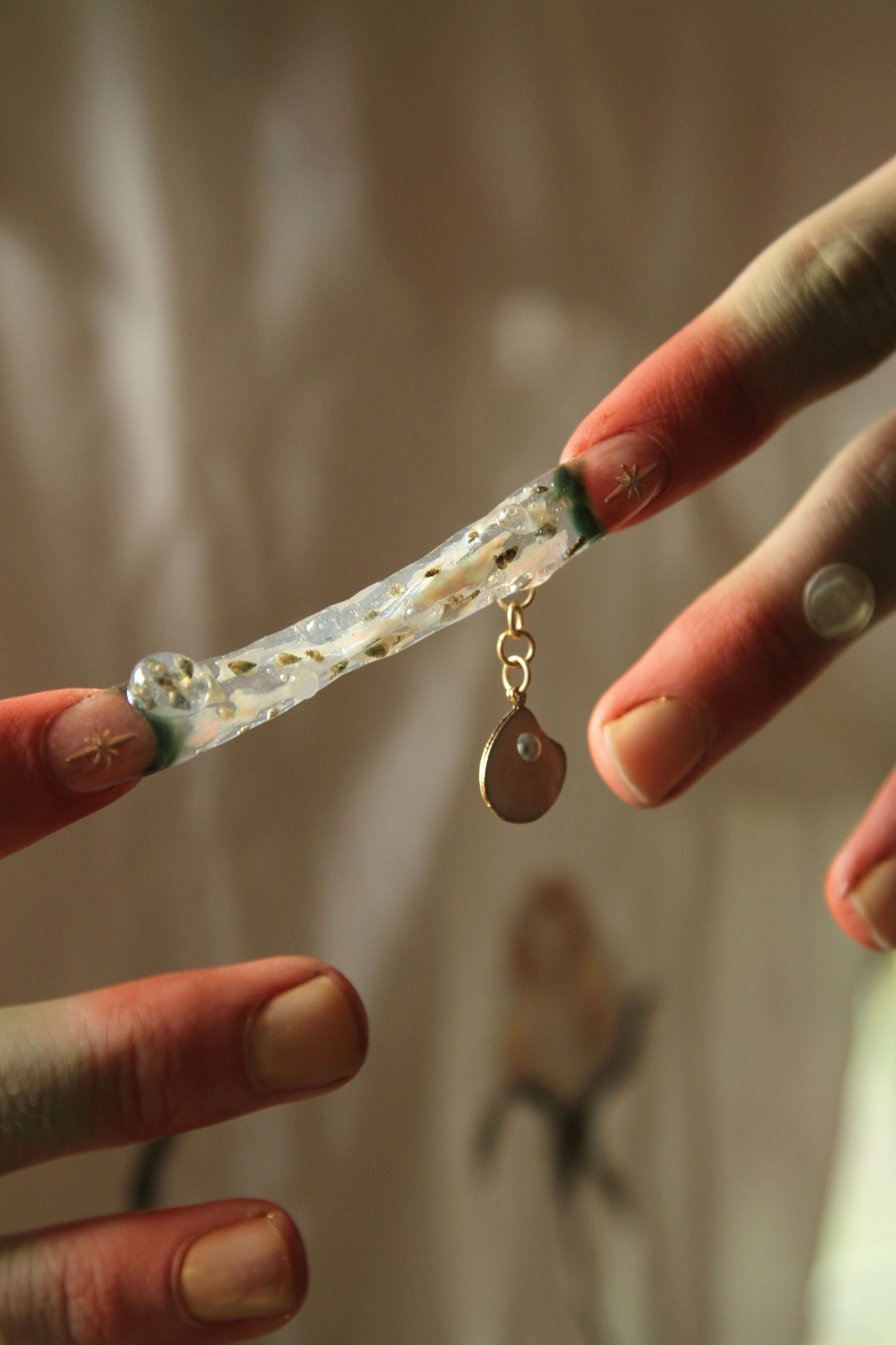 Two pointer fingers connected by a transparent nail sculpture full of tiny snails shining against sunlight